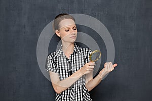 Girl is looking with doubting at her nails through magnifier