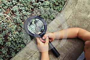 Girl looking at plants grass through magnifying glass.