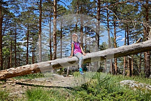 Girl looking at side sitting on fallen tree trunk in forest