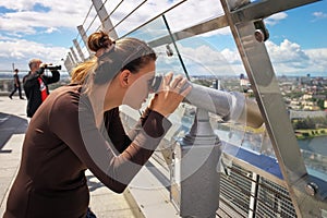 Girl looking through a telescope on the roof of building.