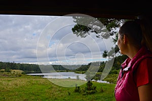 The girl looks at the field and lake among the forest. Cloudy sky and greenery peaceful photo