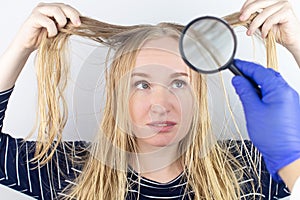 The girl looks in front of the magnifier at her oily hair. Problematic scalp and increased secretion of the sebaceous glands. Hair