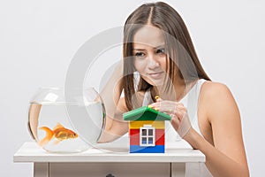 The girl looks at a goldfish and put her hand on the toy house