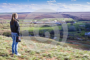 Girl looks from a hill on a rural landscape with drilling rigs in the field