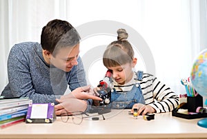 The girl looks through a microscope. Children do biology lessons at home. Home schooling, distance learning during quarantine