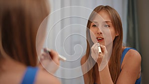 A girl looks in the mirror and paints her lips while standing in a modern apartment. Close-up. Shooting from behind the