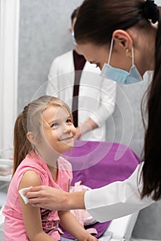 The girl looks at the nurse with a smile and confidence. A young lady doctor is preparing a child for an injection by