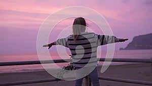 The girl looks at the pink sunset sky on the beach