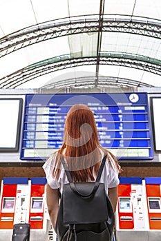 Girl looks on schedule on train station. Back view