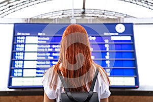 Girl looks on schedule on train station. Back view