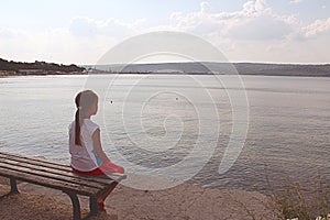 Girl looks at the sea sitting on a bench on the beach