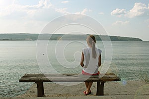 Girl looks at the sea sitting on a bench on the beach