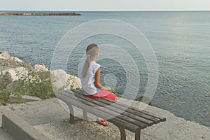 Girl looks at the sea sitting on a bench on the beach