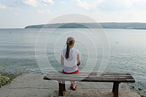 Girl looks at the sea sitting on a bench on the beach