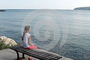 Girl looks at the sea sitting on a bench on the beach