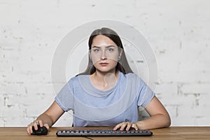 The girl looks straight holding the mouse in her hand and typing on the keyboard