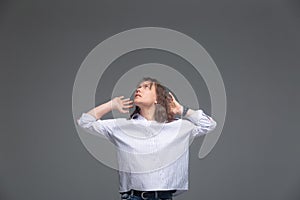 The girl looks to the side with apprehension and tries to cover her ears with her hands on a gray background