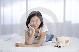A girl lounging with a white Shiba Inu on the bed in the bedroom. Hokkaido inu dog with young woman