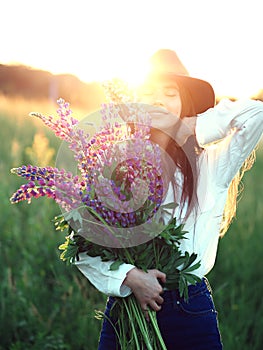 Girl with lupines in shirt and hat at sunset