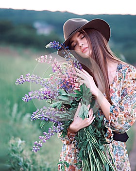 Girl with lupins in a long dress and hat at sunset