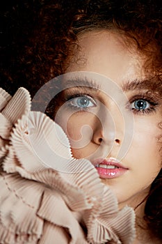 A girl with lush curly red hair. Delicate makeup with false eyelashes in doll style. Ruches cream color.