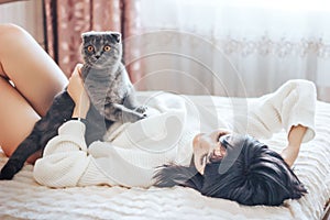 Girl lying on bed with cat pets, comfort, rest and people concept - happy young woman with cat lying in bed at home