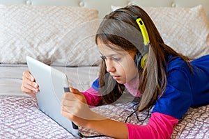 Little girl lying in bed looking at a tablet