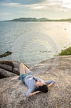 Girl lying on the cliff above seaside at sunset