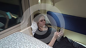 Girl is lying in a compartment car near the window with a phone in her hand and surfing messengers