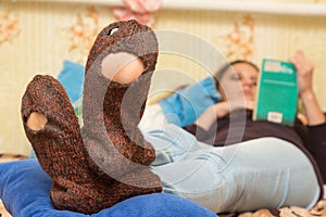 The girl is lying on couch and is reading a book, in the foreground the holey socks photo