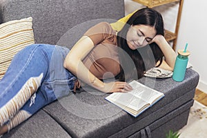 Girl lying on the couch and reads a book. Modern teenager at home. Teen literature concept