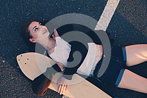 Girl lying down with her longboard on asphalt road and looking away