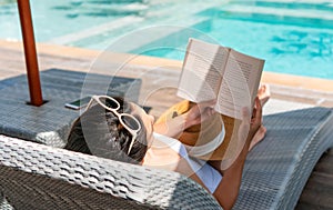 Girl lying down on sunbed while reading a book near Swimming Pool on travel holidays vacation