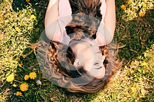 Girl lying on grass with cat on chest. Spring or summer warm weather concept. Bokeh background. Ginger kitten with two face color