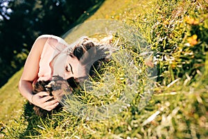 Girl lying on grass with cat. Spring or summer warm weather concept. Bokeh background. Ginger kitten with two face color mask