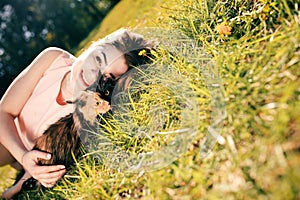 Girl lying on grass with cat. Spring or summer warm weather concept. Bokeh background. Ginger kitten with two face color mask