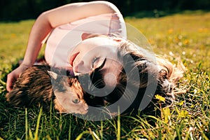 Girl lying on grass with cat. Spring or summer warm weather concept. Bokeh background. Ginger kitten with two face color mask