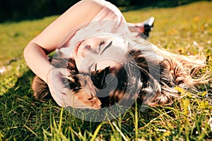 Girl lying on grass with cat. Spring or summer warm weather concept. Bokeh background. Ginger kitten with two face color mask