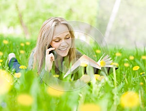 Girl lying on grass with dandelions reading a book and talking