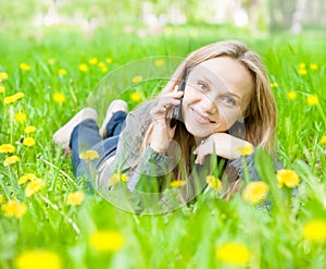 Girl lying on grass with dandelions and talking on the phone