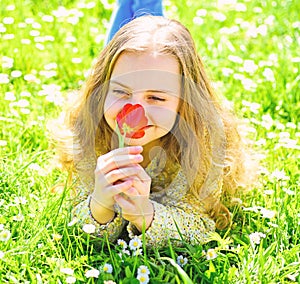 Girl lying on grass, grassplot on background. Girl on smiling face holds red tulip flower, enjoy aroma. Tulip fragrance photo