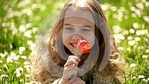 Girl lying on grass, grassplot on background. Tulip fragrance concept. Girl on smiling face holds red tulip flower