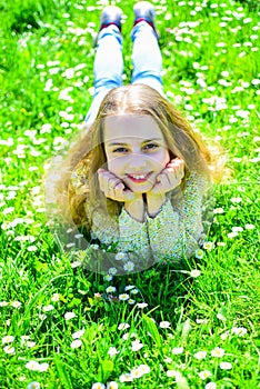 Girl lying on grass at grassplot, green background. Child enjoy spring sunny weather while lying at meadow. Heyday