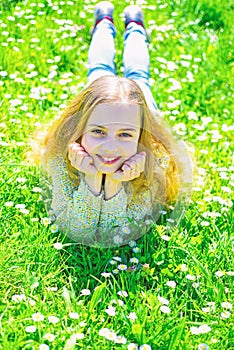 Girl lying on grass at grassplot, green background. Child enjoy spring sunny weather while lying at meadow. Heyday photo