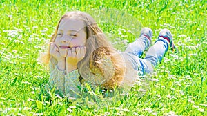 Girl lying on grass at grassplot, green background. Child enjoy spring sunny weather while lying at meadow. Springtime photo