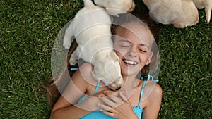 Girl lying in the grass with by her labrador puppy dogs