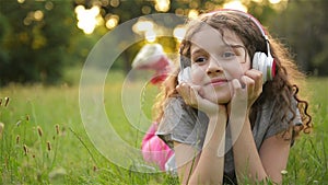 Girl Lying On The Grass And Listening To Music On Headphones. Cute Little Caucasian Kid Is Having Fun Chilling Out