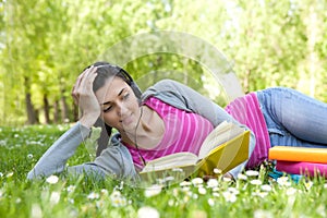 Girl lying on grass in park with book and headset