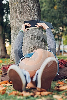Girl lying on the grass, reading a book. Nature, relaxation, purity, education and international book day concept. Unrecognizable
