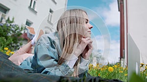 Girl lying in the grass, working with a laptop.